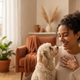 A happy woman in her late 20s with a small dog playfully nudging her hand, conveying relief and satisfaction.